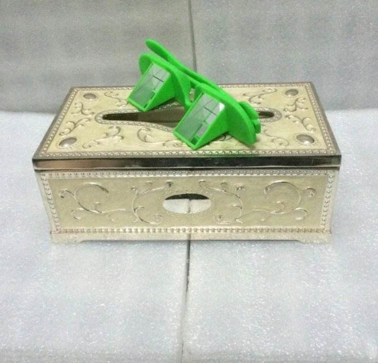 Decorative silver tissue box with ornate design and green prism glasses on top