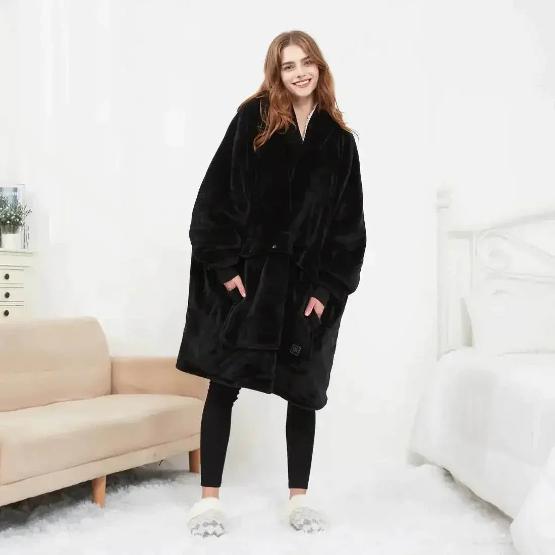 Woman in oversized black fleece hoodie blanket and slippers standing in cozy bedroom