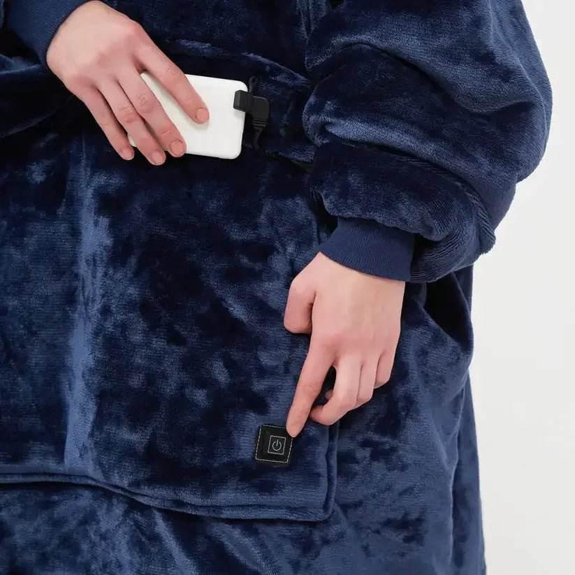 Person wearing plush navy blue heated blanket hoodie, holding power bank, pressing power button