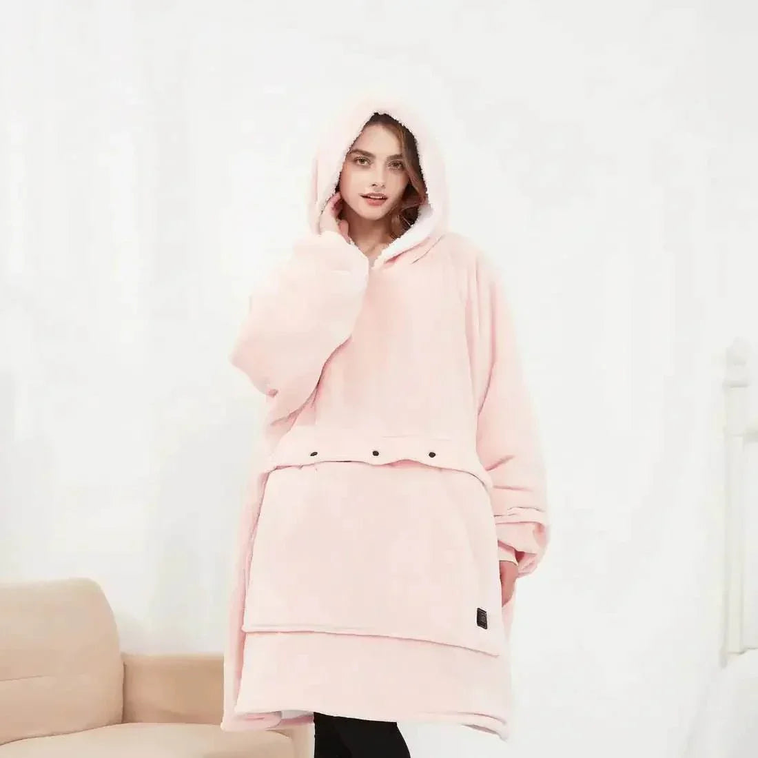 Woman wearing oversized pink hooded blanket sweatshirt in cozy living room setting